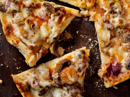 The image shows a close-up of a sliced pizza with toppings that include mushrooms and cheese. The slices are placed on a dark wooden surface.