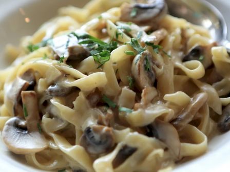 A plate of fettuccine pasta topped with creamy mushroom sauce and garnished with fresh parsley, served with a spoon.