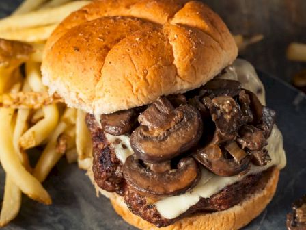 A cheeseburger topped with sautéed mushrooms is plated next to a serving of French fries.