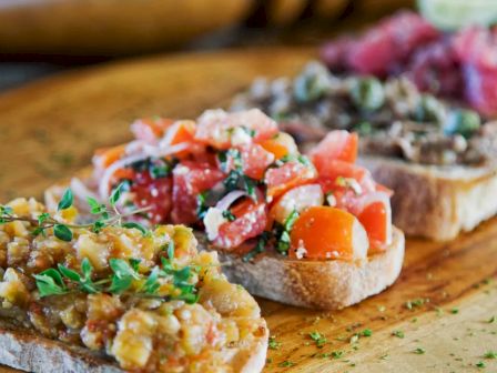 This image shows a wooden board with various types of bruschetta topped with ingredients like tomatoes, herbs, and other savory toppings.