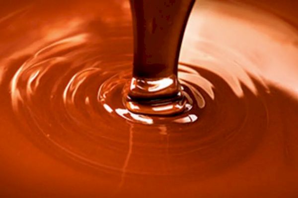 The image shows a close-up of a thick, liquid substance being poured, likely melted chocolate, creating a mesmerizing swirling pattern.