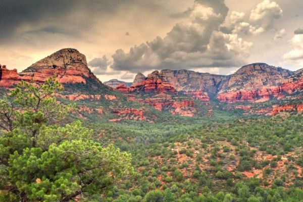 The image shows a scenic landscape with red rock formations, green vegetation, and a cloudy sky, likely depicting a mountainous region.