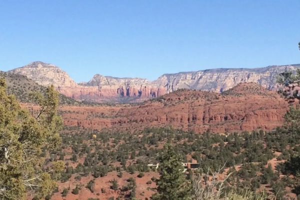 A scenic landscape with red rock formations, green vegetation, and distant mountains under a clear blue sky.