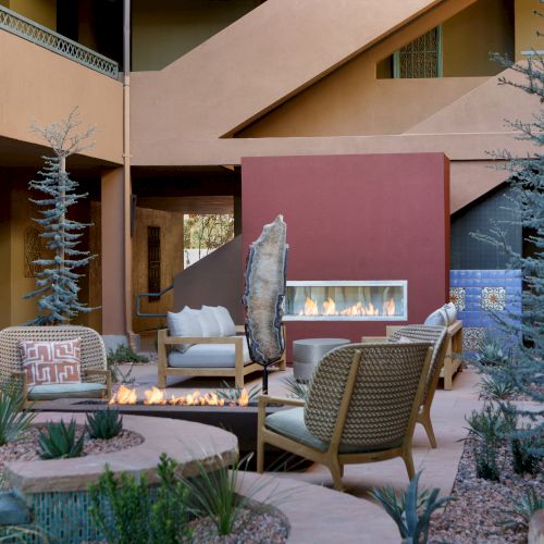 This image features an outdoor seating area with modern chairs, a central fire pit, and minimalist landscaping, set against a warm-colored architectural backdrop.