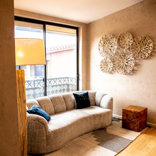 A cozy living room with a gray sofa, abstract wall decor, a rug, a side table, and a floor lamp. Natural light fills the space through a window.