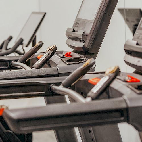 The image shows several treadmills lined up in a gym or fitness center, each equipped with digital screens for tracking workouts.