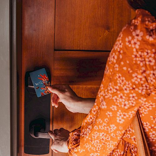 A person wearing an orange floral top is using a key card to unlock a wooden door, highlighting a modern electronic lock system.