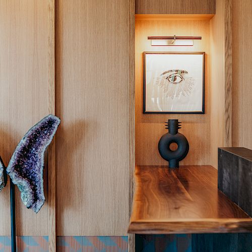 A modern interior with wooden panels, a purple geode decoration, a small sculpture, and a framed sketch of an eye illuminated by a small light.