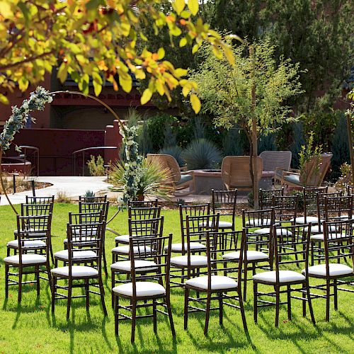 The image depicts an outdoor setup with rows of chairs on a grassy area, likely for an event, with an archway and trees in the background.