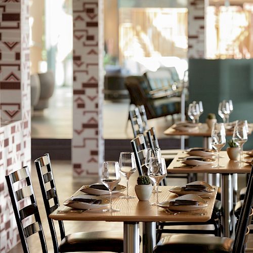 The image shows a well-lit, modern restaurant interior with neatly arranged tables and chairs, set with glasses, napkins, and cutlery.