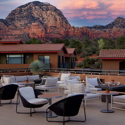 A beautiful patio with modern seating overlooks stunning red rock formations and buildings under a colorful sky.