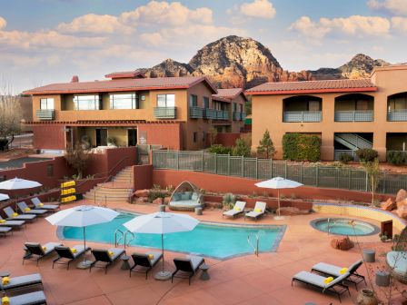 A resort with a pool, lounge chairs, umbrellas, and a hot tub against a backdrop of mountains and a clear sky ending the sentence.