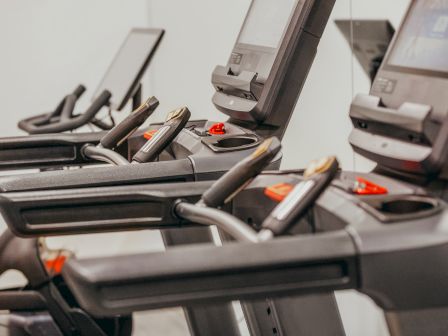 The image shows several treadmills in a gym, lined up side by side, with screens and control panels visible on each treadmill.