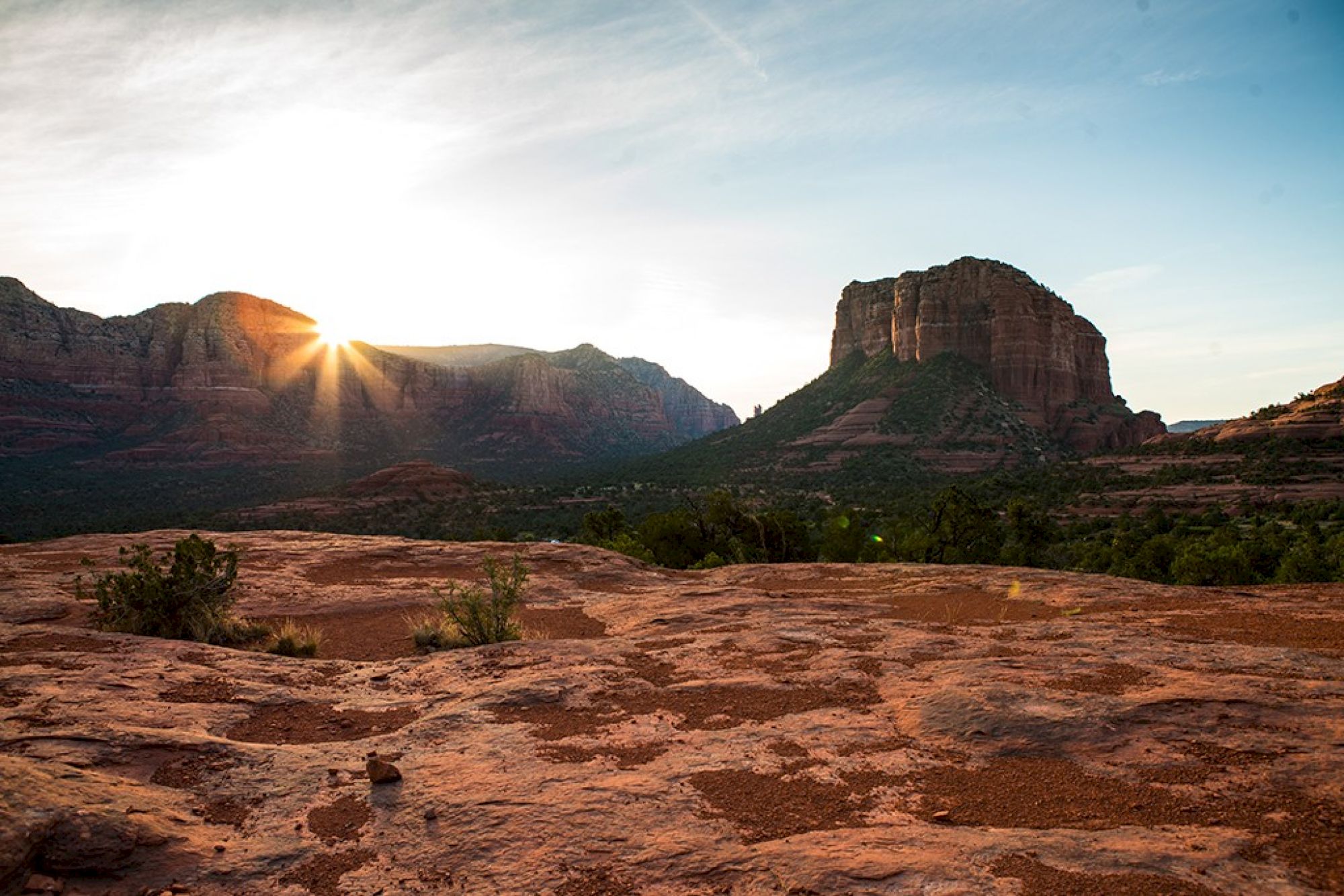 A scenic landscape featuring a sunset or sunrise over rocky mountains and a reddish desert foreground.