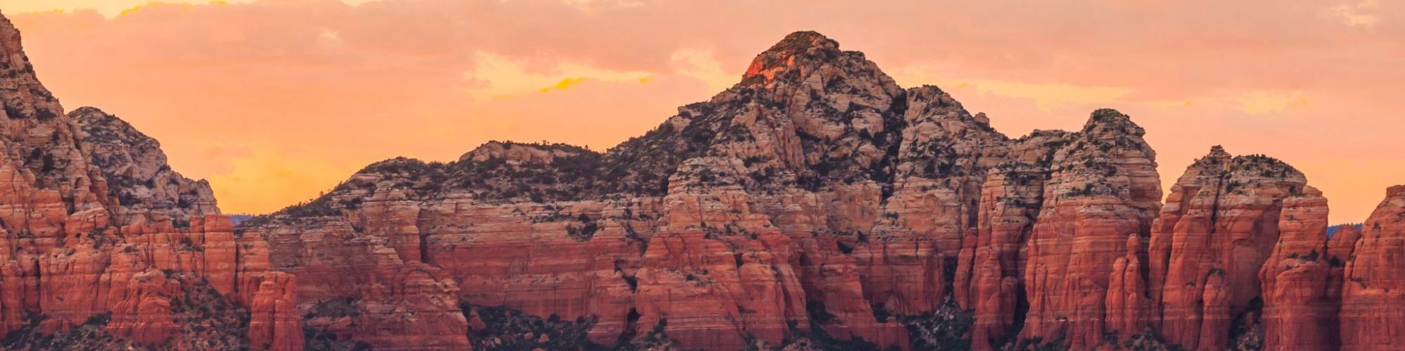 A picturesque view of a mountainous landscape at sunset, featuring red rock formations and a serene valley below, with a colorful sky.