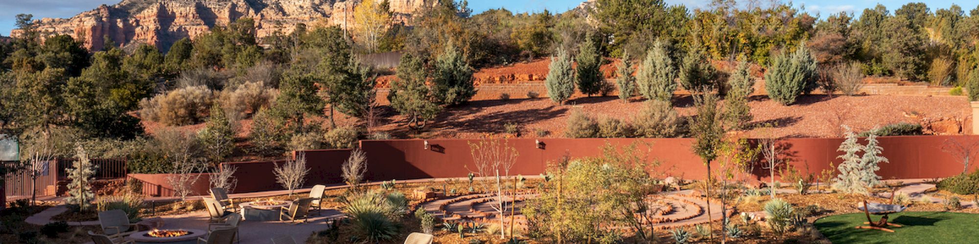 An outdoor area with fire pits, chairs, hammocks, desert landscaping, and a mountain in the background under a blue sky with some clouds.