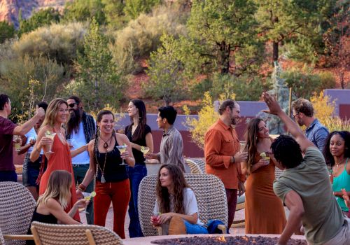 A group of people are gathered outdoors, socializing and enjoying drinks. The setting appears to be a casual, scenic, and relaxed environment.