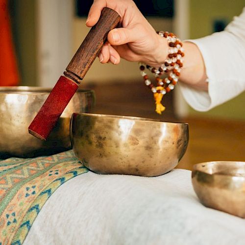 A person is using a mallet to play Tibetan singing bowls placed on a cloth-covered surface, likely for a sound healing session.