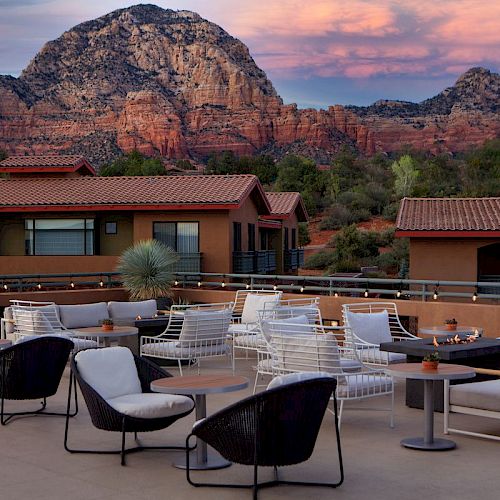 An outdoor seating area features modern furniture with mountains and a pink-tinged sky in the background, creating a serene and picturesque setting.