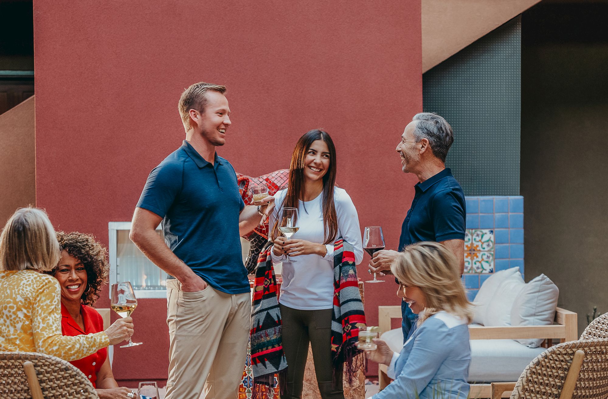 A group of people in casual attire are enjoying drinks and socializing outdoors, appearing relaxed and happy with each other.