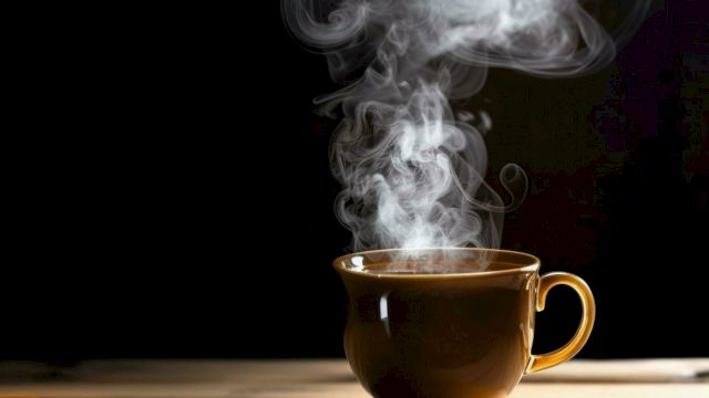 A steaming cup of coffee sits on a wooden table, with steam rising elegantly against a dark background.