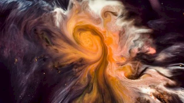 The image shows a swirl of vibrant colors, primarily oranges, and yellows, resembling a cosmic nebula against a dark background.