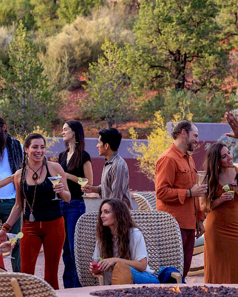 A group of people are gathered outdoors, socializing and enjoying drinks. The setting appears to be a casual, scenic, and relaxed environment.