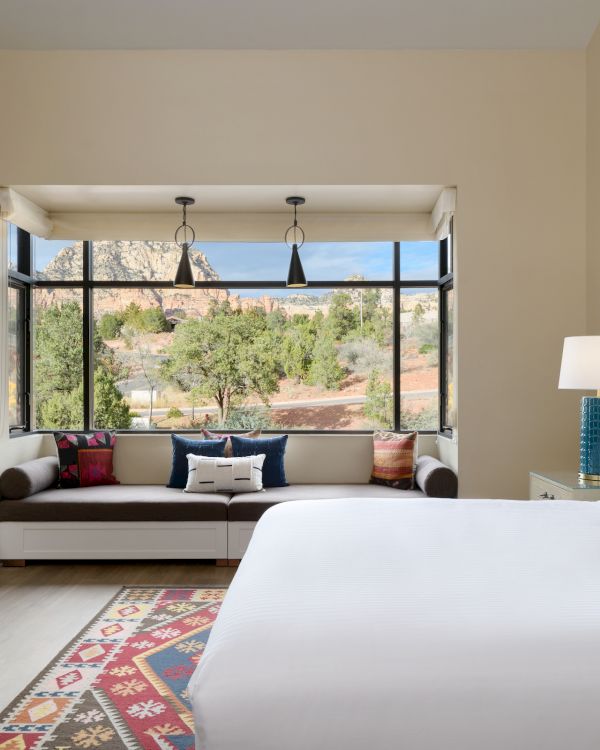 A cozy bedroom with a large bed, patterned rug, and a seating area with a view of the outdoors through large windows.