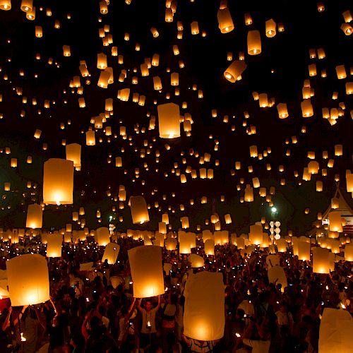 A crowd releases glowing lanterns into the night sky, creating a magical and illuminated scene during a lantern festival.