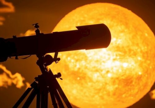 A telescope is silhouetted against a large, bright image of the sun in a dramatic sunset scene.