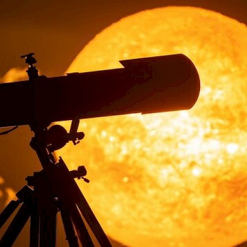 A telescope is silhouetted against a large, bright image of the sun in a dramatic sunset scene.
