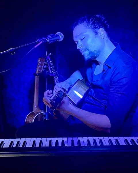 A person is playing guitar under blue lighting, with a microphone and keyboard nearby, creating a musical atmosphere.