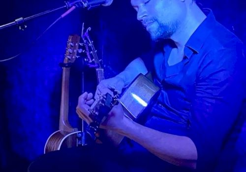 A person is playing guitar under blue lighting, with a microphone and keyboard nearby, creating a musical atmosphere.